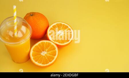 Orange juice in a plastic glass with a straw. Sliced orange on a yellow Stock Photo