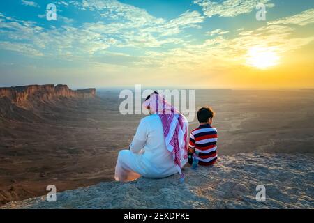 An arab man and his son sitting on Edge of the world, a natural landmark and popular tourist destination near Riyadh -Saudi Arabia.08-Nov-2019. Select Stock Photo