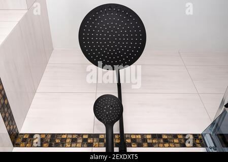A modern, black metal shower with small and large rain shower, placed on tiles. Stock Photo