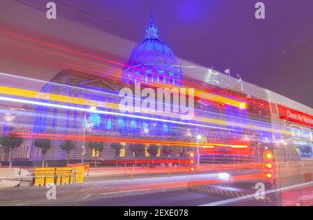 Electrical bus pass on street as San Francisco City Hall lights up in blue to honor the healthcare workers during COVID-19 pandemic, California, USA. Stock Photo