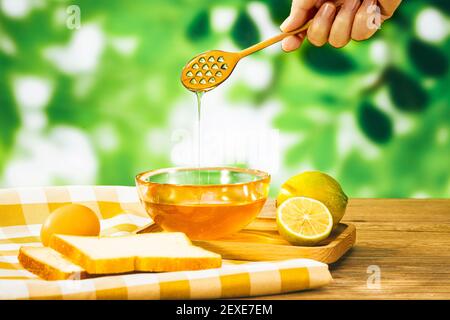A closeup of a hand holding a wooden dipper with honey pouring into a bowl next to rustic products Stock Photo