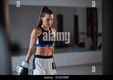Portrait of a young attractive girl boxer in the gym wearing gloves next to a punching bag Stock Photo
