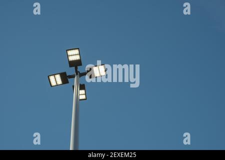 A view looking straight up at street lights from below shows the pole and light fixture against a solid blue sky. Stock Photo