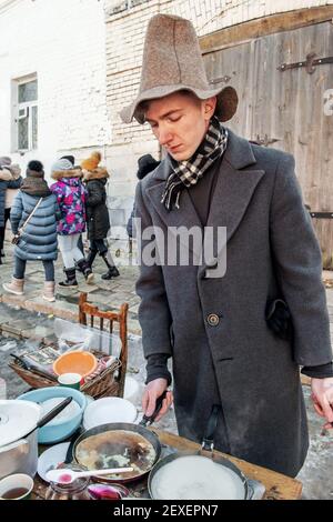 March 10, 2019 Kolomna, Russia: a young man in a high hat bakes pancakes on the street. Celebration of Maslenitsa in Russia. Stock Photo