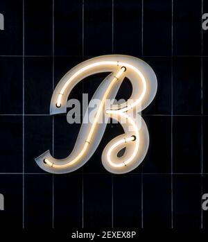 White neon letter B in cursive on black tiles Stock Photo