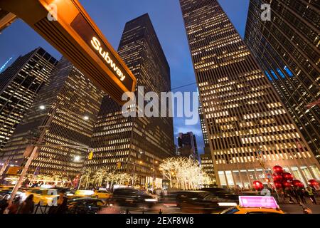 Midtown Sixth Avenue traffic goes through among the rows of high-rise buildings during the Christmas Holiday Season in the night at New York City NY. Stock Photo