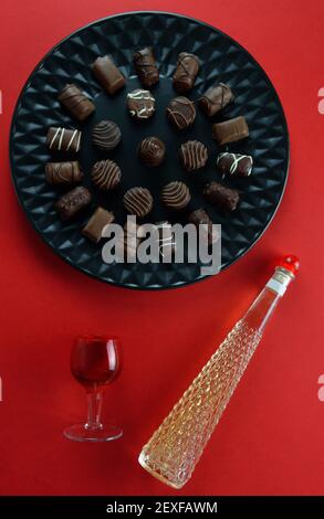 Various chocolate pralines on black plate , a red glass and a bottle with liquor on red background Stock Photo