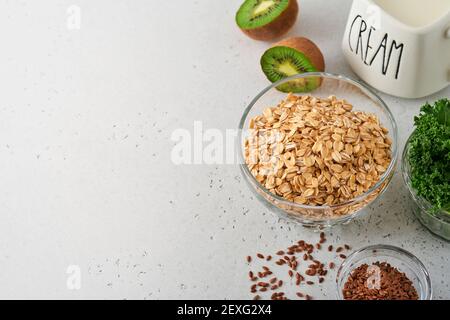 Oatmeal, kale, kiwi and chia seeds, cream ingredients for making detox smoothies on gray light concrete background. Selective focus. Mock up. Stock Photo