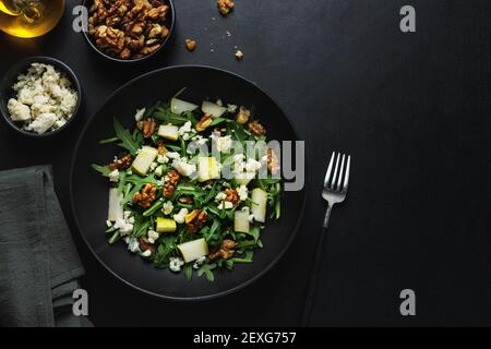 Tasty appetizing salad with pear, blue cheese, walnuts, arugula served on dark plate. Stock Photo