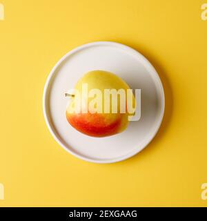single ripe apple on white plate on yellow background, top view Stock Photo