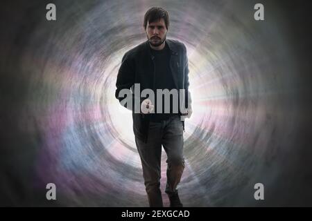 Young man is running away from death. Bright gods rays in tunnel in background. Stock Photo