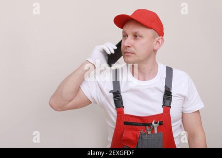 construction male worker In red working form and cap with cellphone in hand and communicates with customers isolated on white background. of the servi Stock Photo