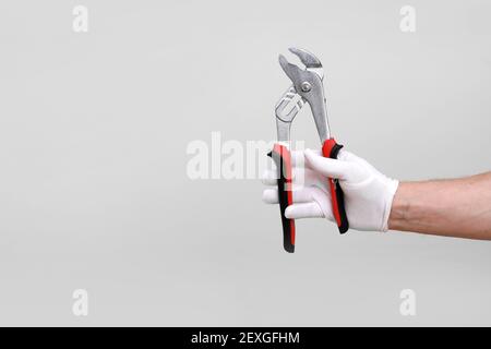 Man's hand in white glove raised holding a black and red tool: pliers, wire cutter. Isolated on white background. Open, clean, ready to cut form. Mock Stock Photo