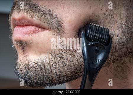 Facial hair care concept. Young man is using derma roller  on beard. Stock Photo