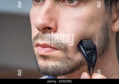 Facial hair care concept. Young man is using derma roller  on beard. Stock Photo