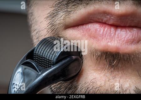 Facial hair care concept. Young man is using derma roller  on beard. Stock Photo