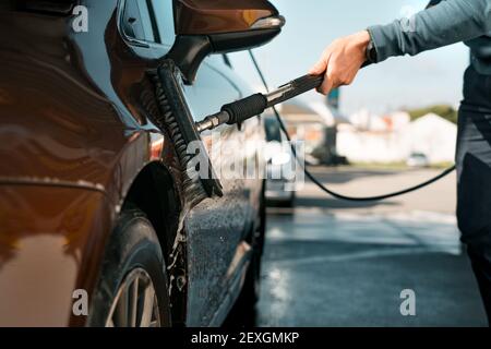 Washing automobile with a brush in self serve car wash. Cleaning car outdoors at car washing station. Smart wash. Stock Photo