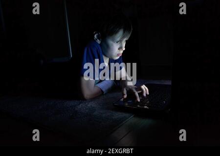 portrait of boy using laptop in dark room Stock Photo