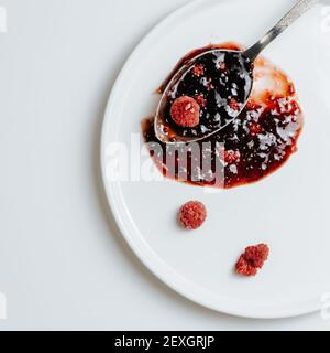 Spoon of raspberry jam on a white plate with frozen berries Stock Photo