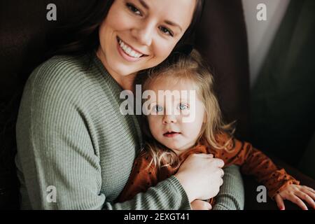 Young girl and her mother snuggle together on a chair in nursery Stock Photo