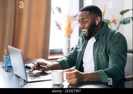 Satisfied friendly African American successful male freelancer or businessman looking at the laptop happily, got a good message or made a good deal Stock Photo