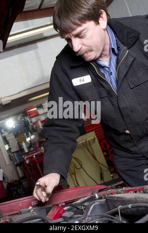 Automotive Technician Works Under the Car Hood in Auto Repair Stock Photo