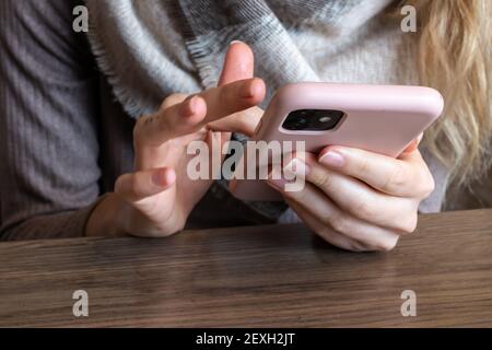 Woman with a finger tattoo and blonde hair scrolling on her pink smartphone rapidly in a cafe, February 2021. Stock Photo