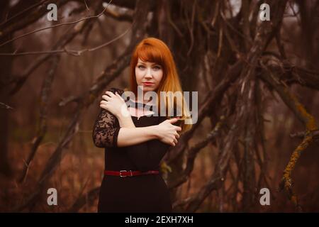 Red-haired model girl in black woman dress dry autumn dark fores Stock Photo