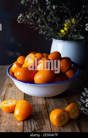 Fresh kumquats in the plate on the natural wooden background. Cumquat or kumquat. Stock Photo