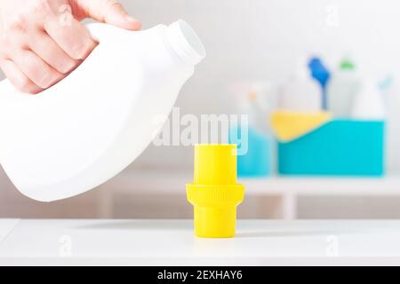 White chlorine bottle with yellow cover mock-up. Toxic detergent. Cleaning supplies in background. Using of measuring cup. Stock Photo