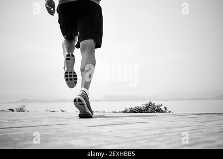 close-up shot of legs of an asian runner running by the sea, rear view, black and white Stock Photo