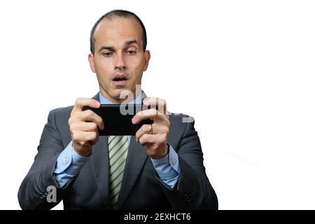 Mature man with suit and tie, playing on his smartphone and with surprised face. Stock Photo