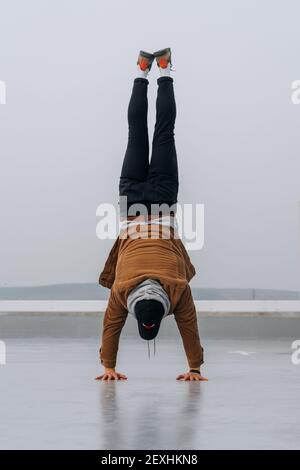 A vertical shot of a man doing a handstand outdoors on a gloomy day Stock Photo