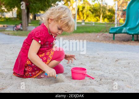 Little girl playing in the sandbox with shovel and bucket in the park in summer. Stock Photo