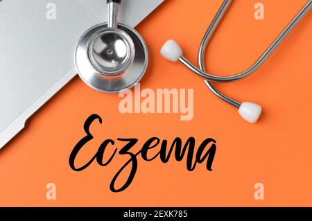 Stethoscope and notebook over orange background written with ECZEMA. Stock Photo