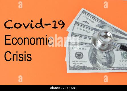 Stethoscope and money banknotes over orange background written with COVID-19 ECONOMIC CRISIS. Stock Photo