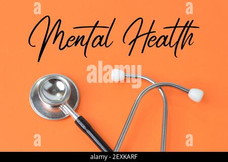 Stethoscope over orange background written with text MENTAL HEALTH. Stock Photo