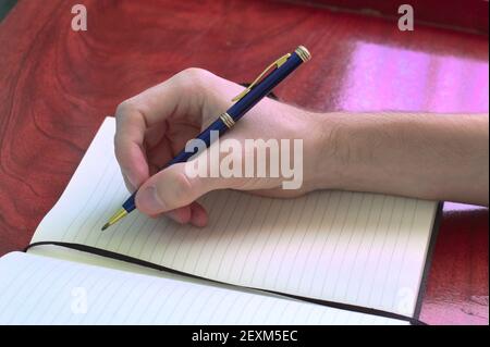A closeup shot of a male hand with pen writing on a notebook Stock Photo