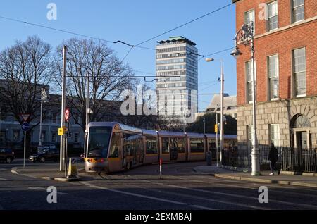 DUBLIN, IRELAND - Jan 15, 2020: The Luas electric modern tram at the street bend in Dublin city center on sunny winter day. The Liberty Hall high buil Stock Photo