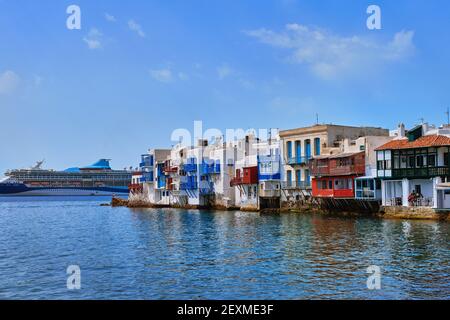 Beautiful Little Venice in Mykonos, Greece. Romantic neighborhood with whitewashed bars, cafes, restaurants. Giant cruise liner pass. Summer day. Stock Photo