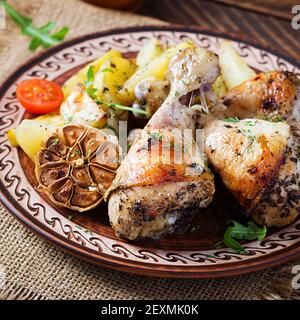 Baked chicken legs with slice potatoes and herbs. Barbecue chicken drumsticks on wooden table. Stock Photo