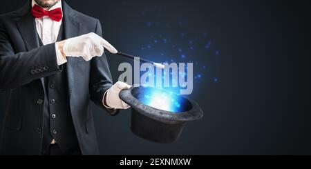 Magician or illusionist is showing magic trick with wand and hat on dark background. Stock Photo