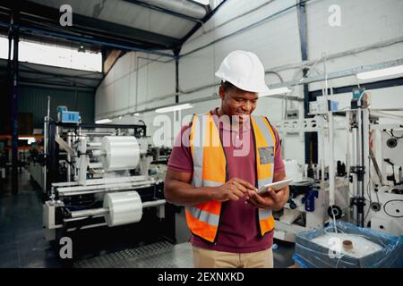 Smiling young african male employee using digital tablet while working in industry Stock Photo