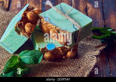 A fragrant green organic handmade soap decorated with mint leaves and burlap on a brown wooden countertop. Stock Photo
