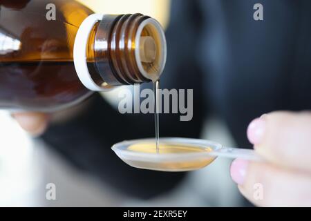 Woman pouring medicinal syrup into measuring spoon closeup Stock Photo