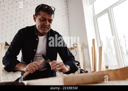 Middle-aged man carpenter working in a workshop with chisel and hammer Stock Photo