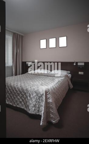 Interior of a comfortable hotel bedroom in the morning in luxury style. Big window. Black wooden photo frames mockup, interior decor Stock Photo