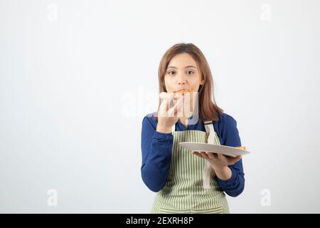 Adorable young girl in apron eating pizza on white background Stock Photo