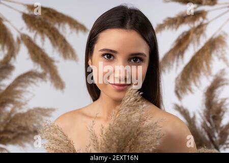 Caucasian model posing on gray background with dry pampas grass reeds. Minimal, stylish, monochrome concept. Neutral colors, cute pattern. Decorative Stock Photo