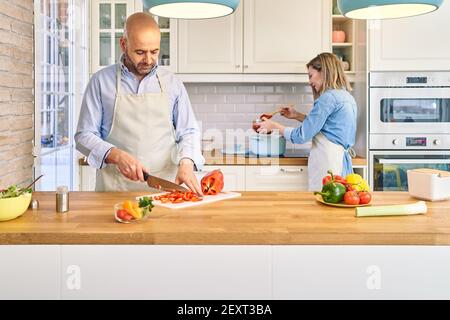 A happy young couple is enjoying and preparing a healthy meal. He cuts vegetables, she cooks spaghetti. . High quality photo Stock Photo